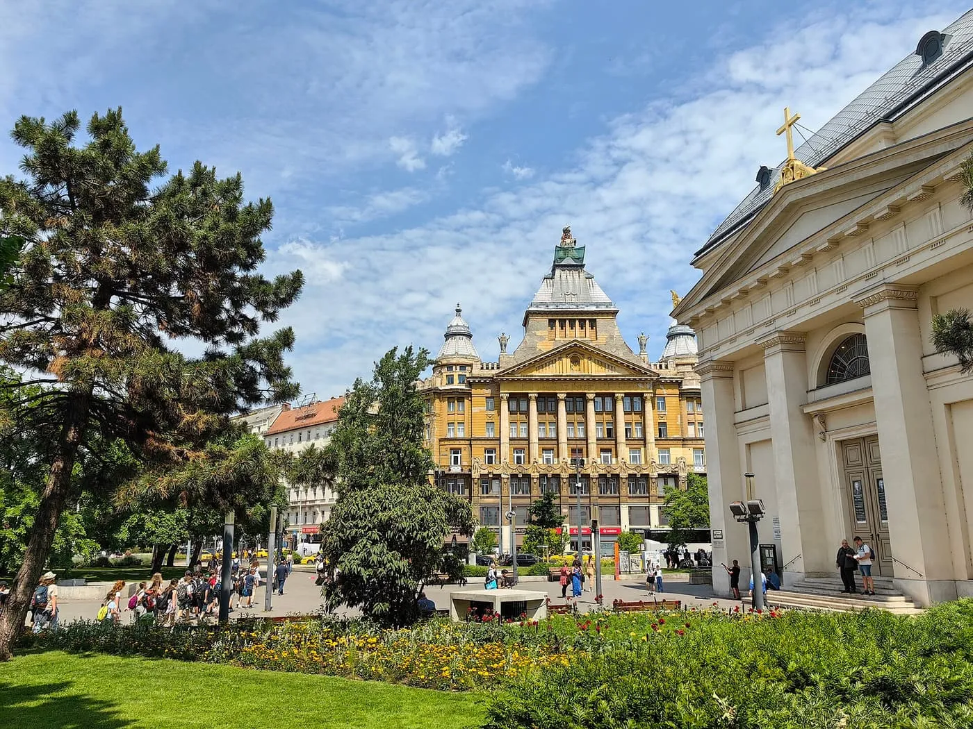 Deák Ferenc tér in sunshine, with a church portico on the right and the Anker Palace behind the trees