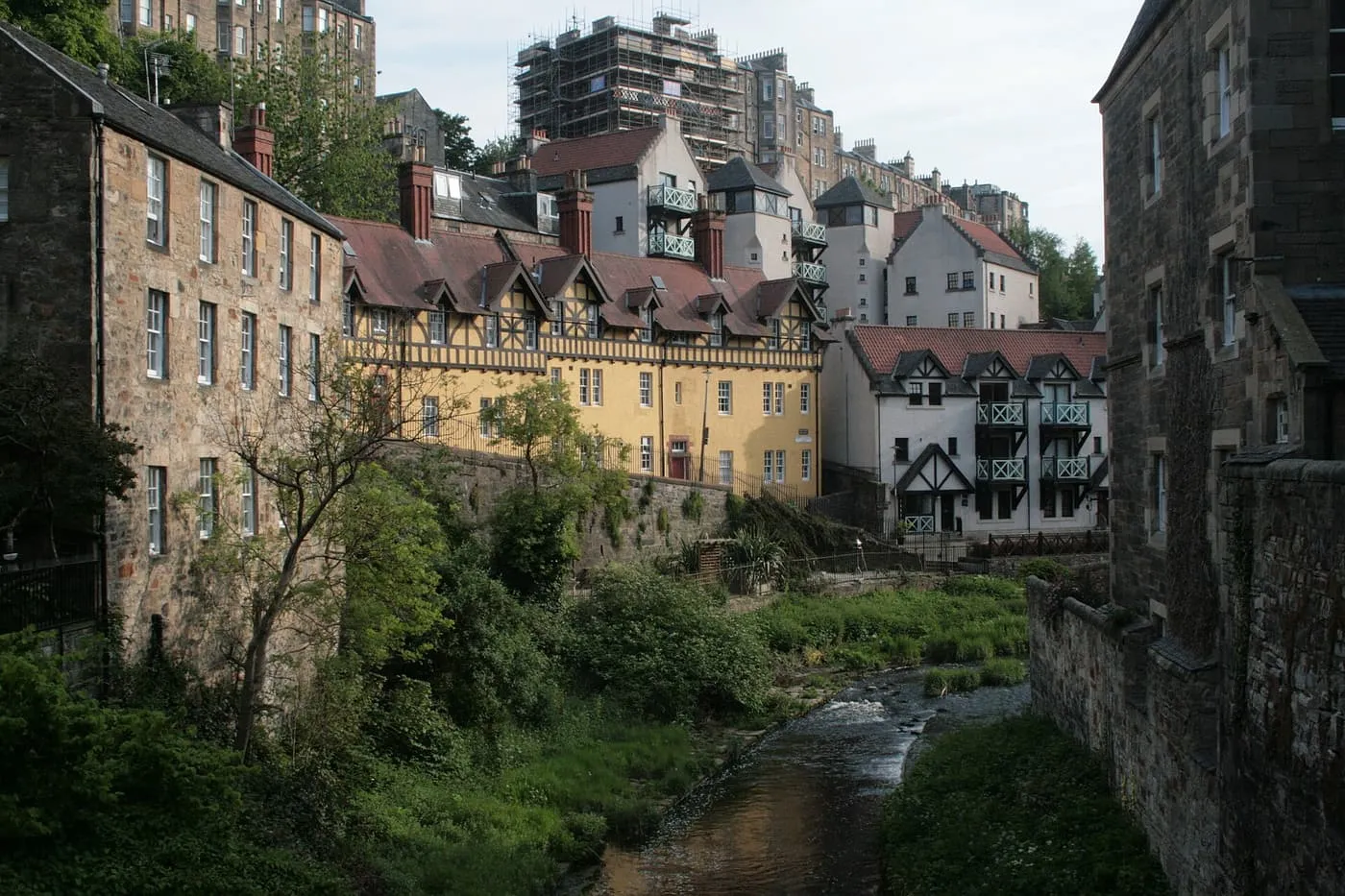 Half-timbered and stone houses above the Water of Leith at Dean Village, with green banks along the stream
