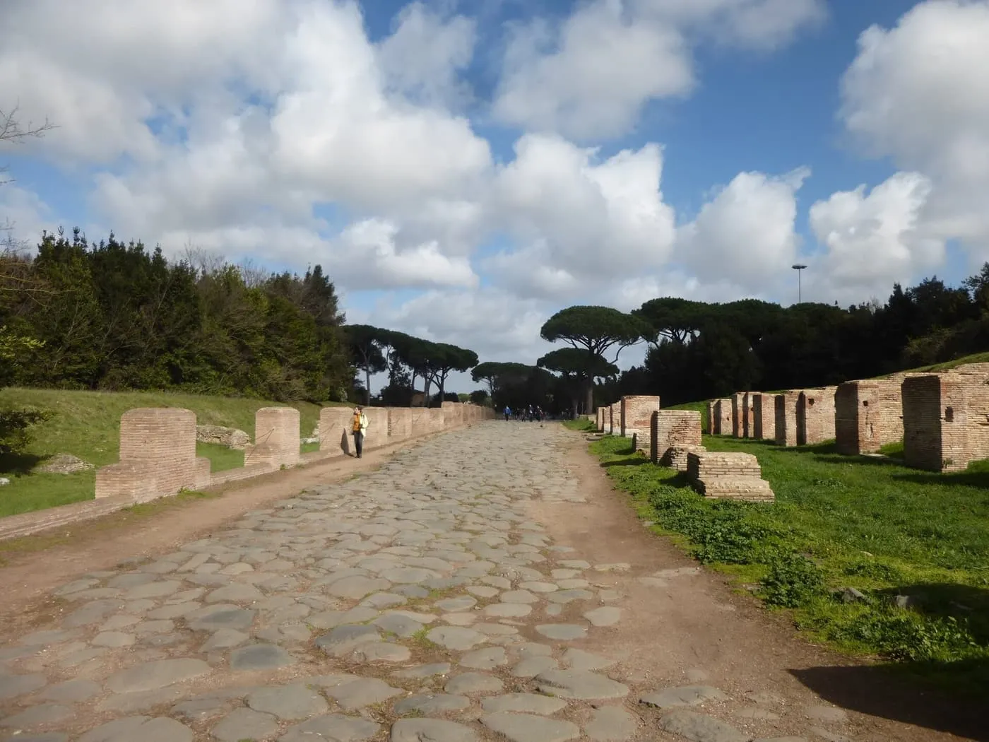 The paved Decumanus, Ostia's main street, running between low brick ruins towards umbrella pines