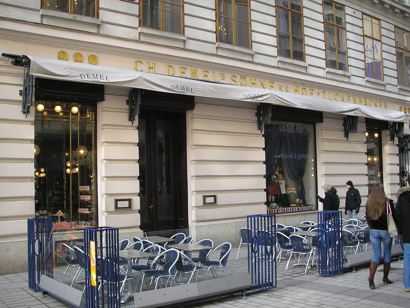 The white Kohlmarkt frontage of Demel, with the gold DEMEL lettering over the windows and a glass-fenced terrace of tables in front