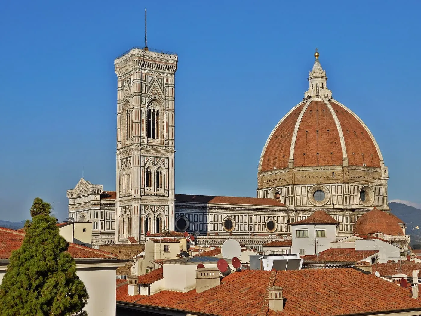 Giotto's Bell Tower and the red-tiled dome of Florence Cathedral rising above the rooftops under a blue sky