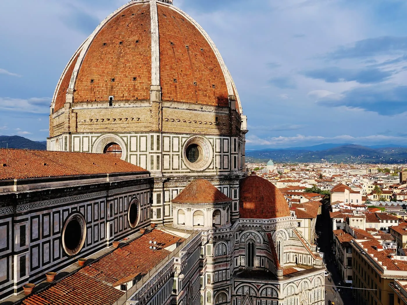 The red dome of Florence Cathedral and the marble flank of the nave seen from the Bell Tower, with the city and hills beyond