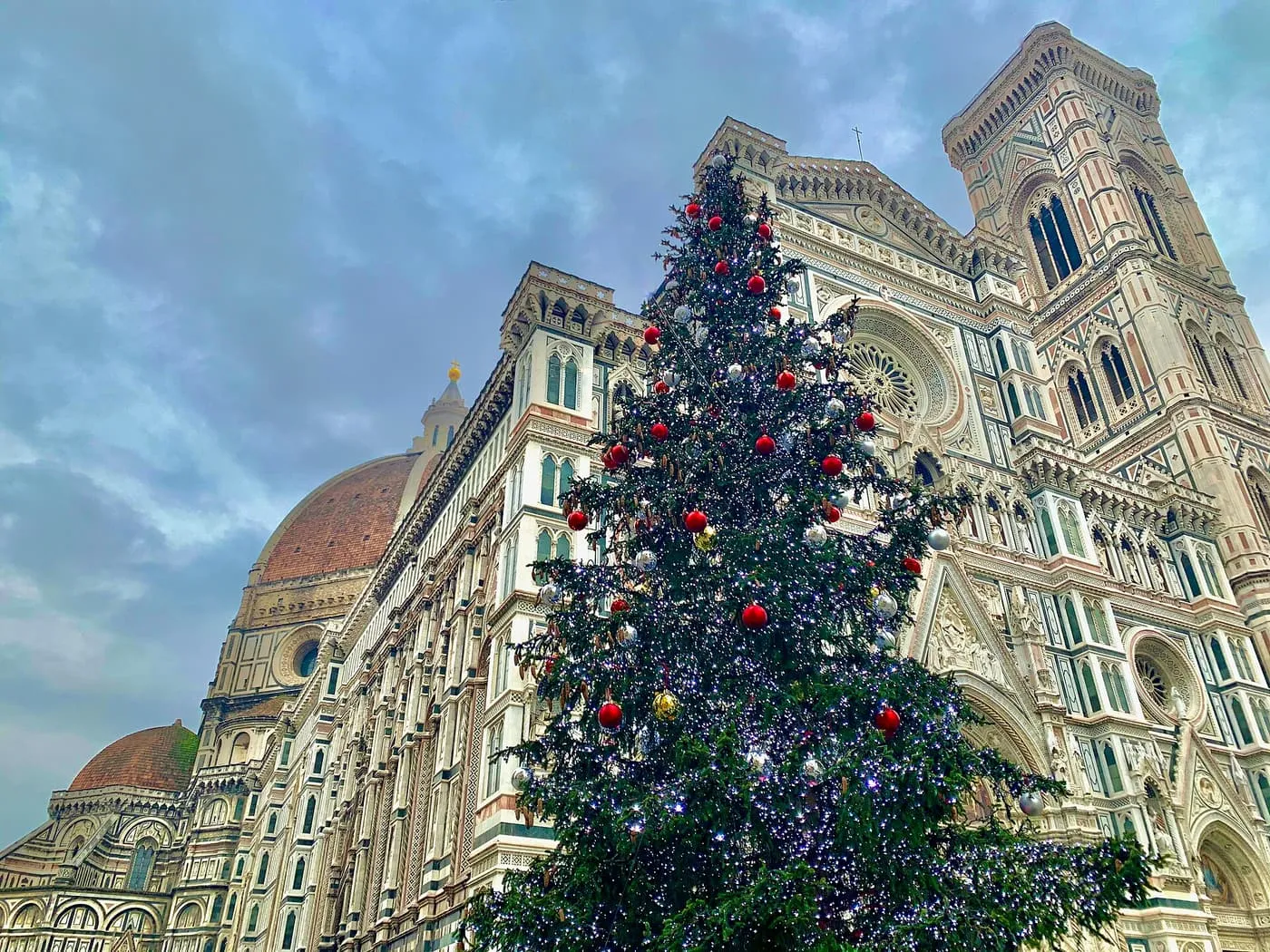 A tall Christmas tree hung with red baubles in front of the cathedral, with Giotto's Bell Tower on the right