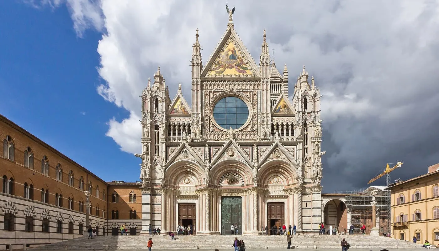 The striped marble front of Siena Cathedral with its round window and gold mosaic gables