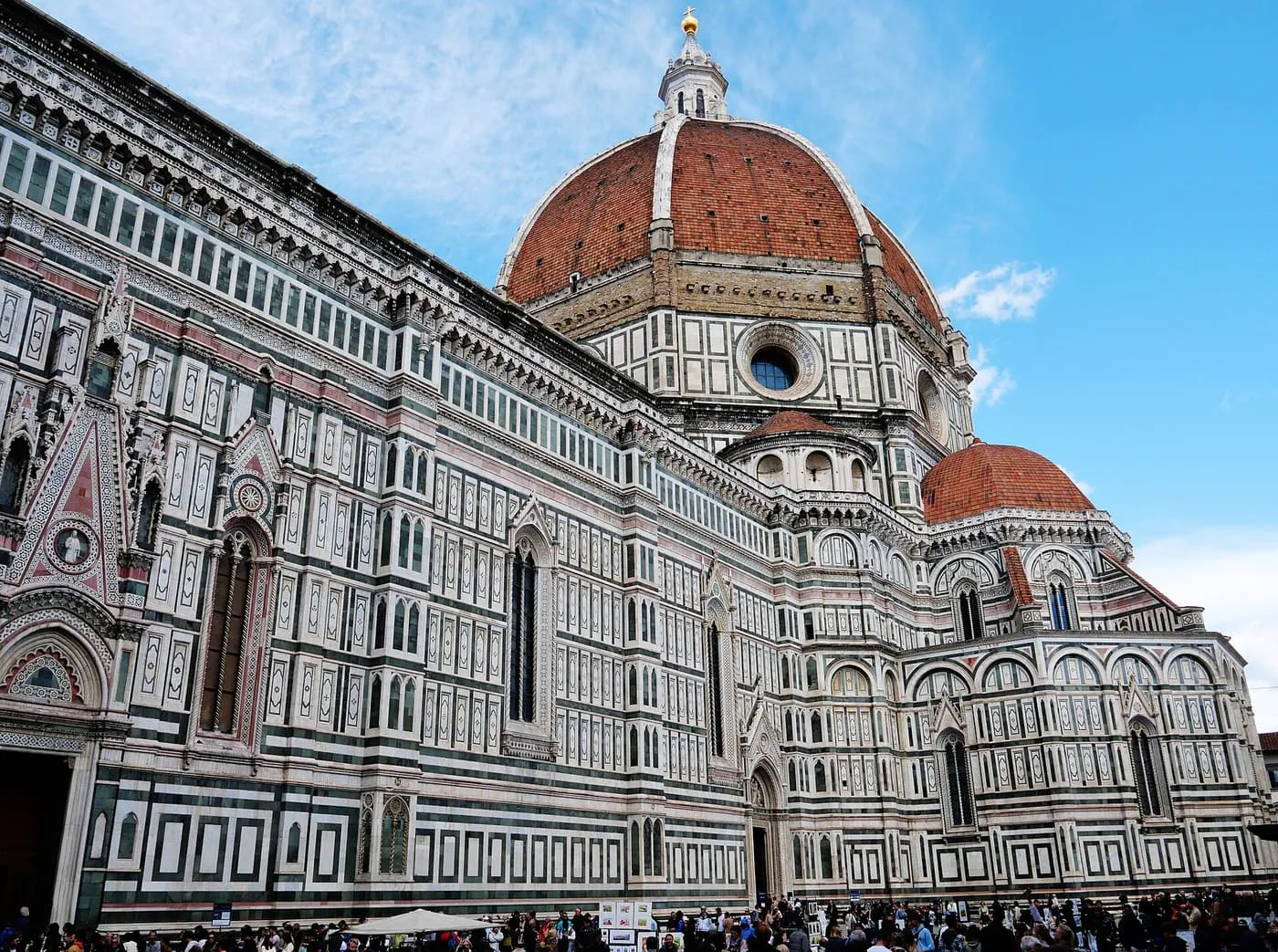 The south side of Florence Cathedral in white, green and pink marble, with the red dome rising behind the nave