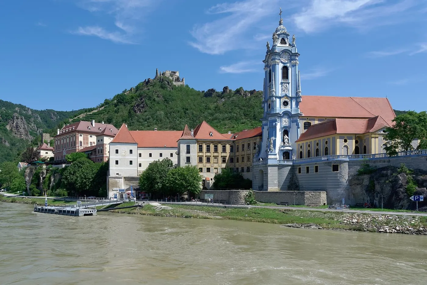 The blue baroque tower of Dürnstein Abbey above the Danube, with the castle ruin on the hill behind