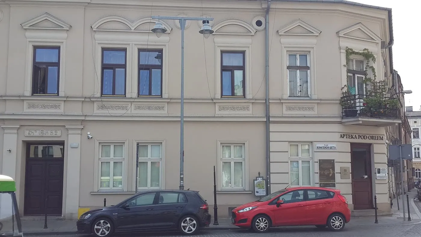 The front of the Eagle Pharmacy, a cream two-storey building with the sign "Apteka pod Orłem" on the corner of Ghetto Heroes Square