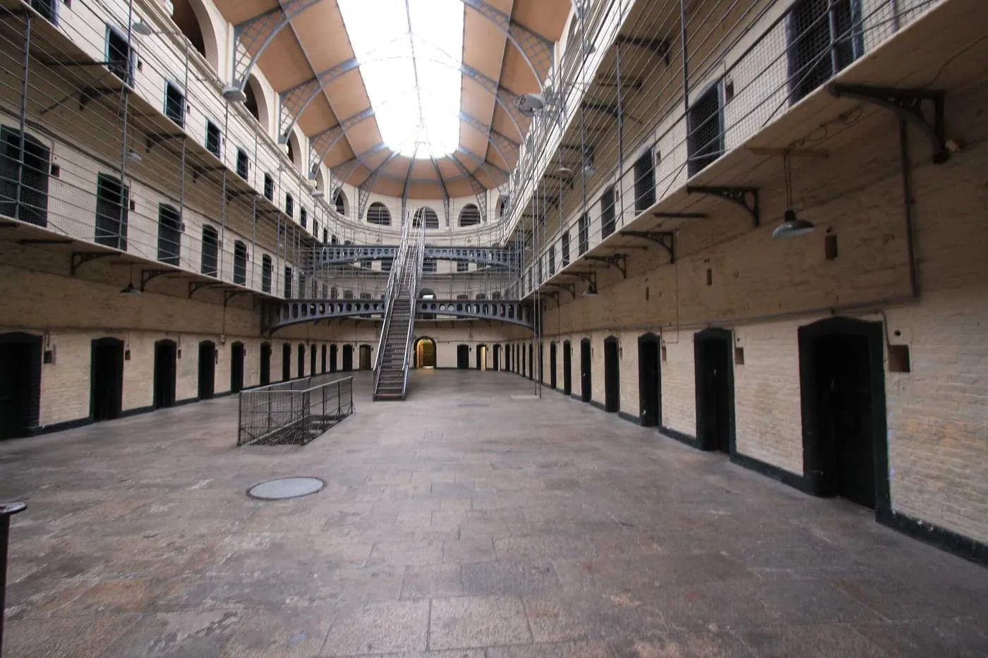 The East Wing hall at Kilmainham Gaol, with tiers of cell doors, iron landings and a staircase beneath a pitched glass roof