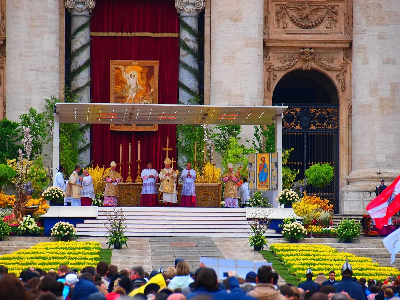 An Easter Mass on the altar platform in front of St Peter's Basilica, with rows of yellow flowers and a crowd in the square