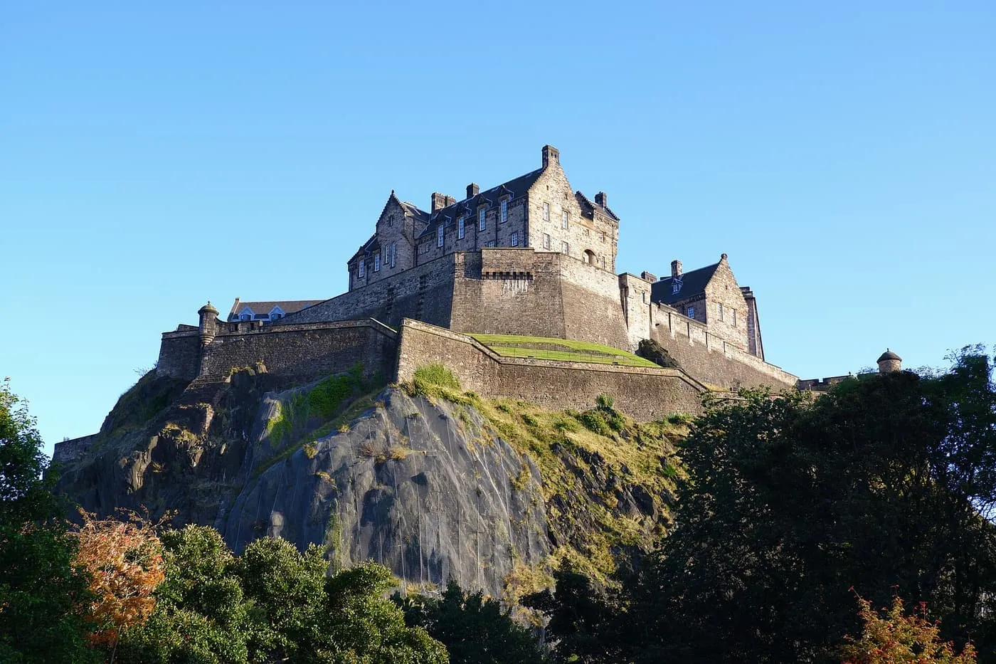 Edinburgh Castle on its rock in low sun, with orange autumn leaves in the trees below