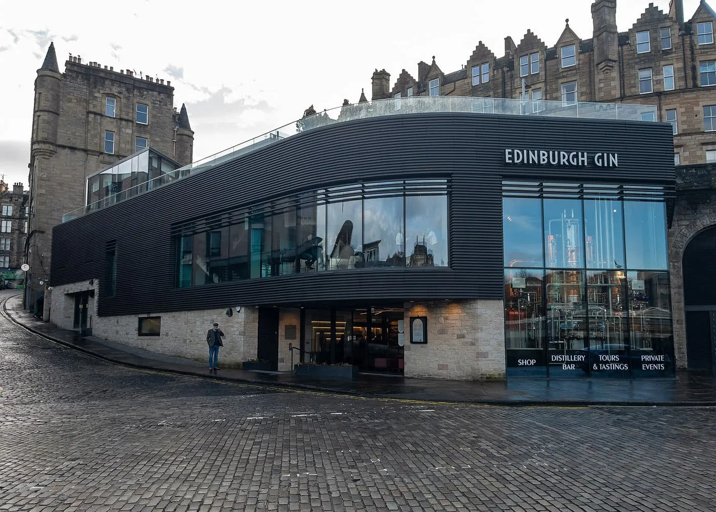 The black and glass front of the Edinburgh Gin distillery on a cobbled corner, with distilling equipment visible through the windows