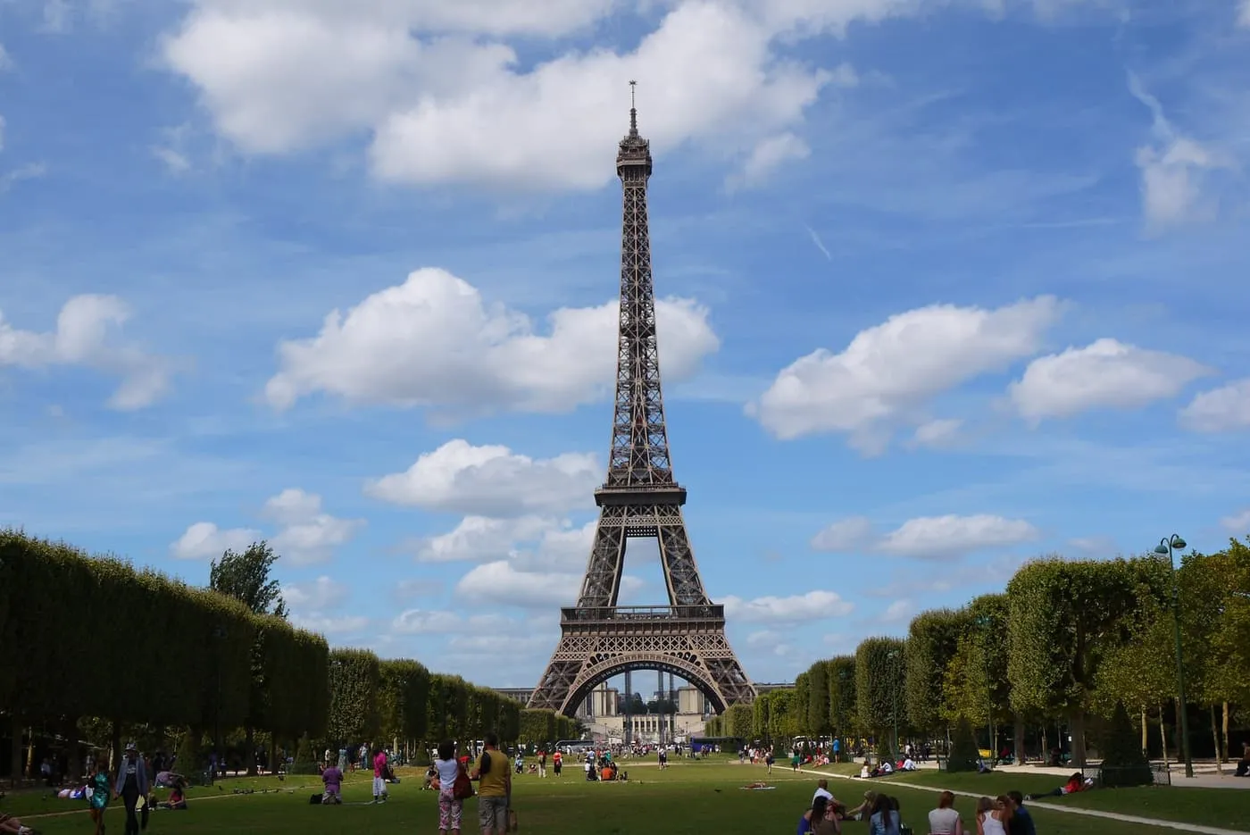 The Eiffel Tower seen down the lawns of the Champ de Mars under a blue sky with clouds