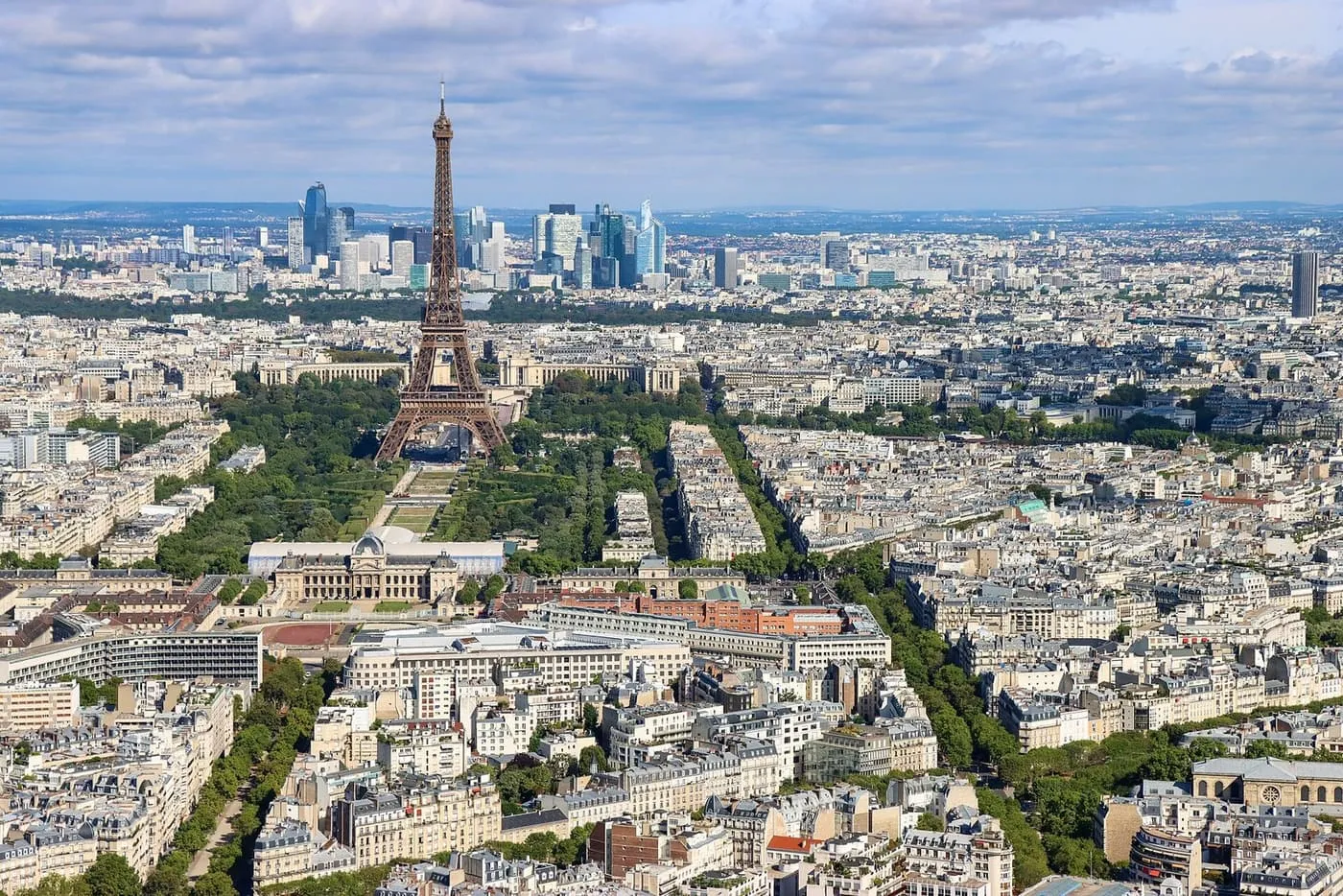 The Eiffel Tower and the Champ de Mars seen from above, with the towers of La Défense on the horizon