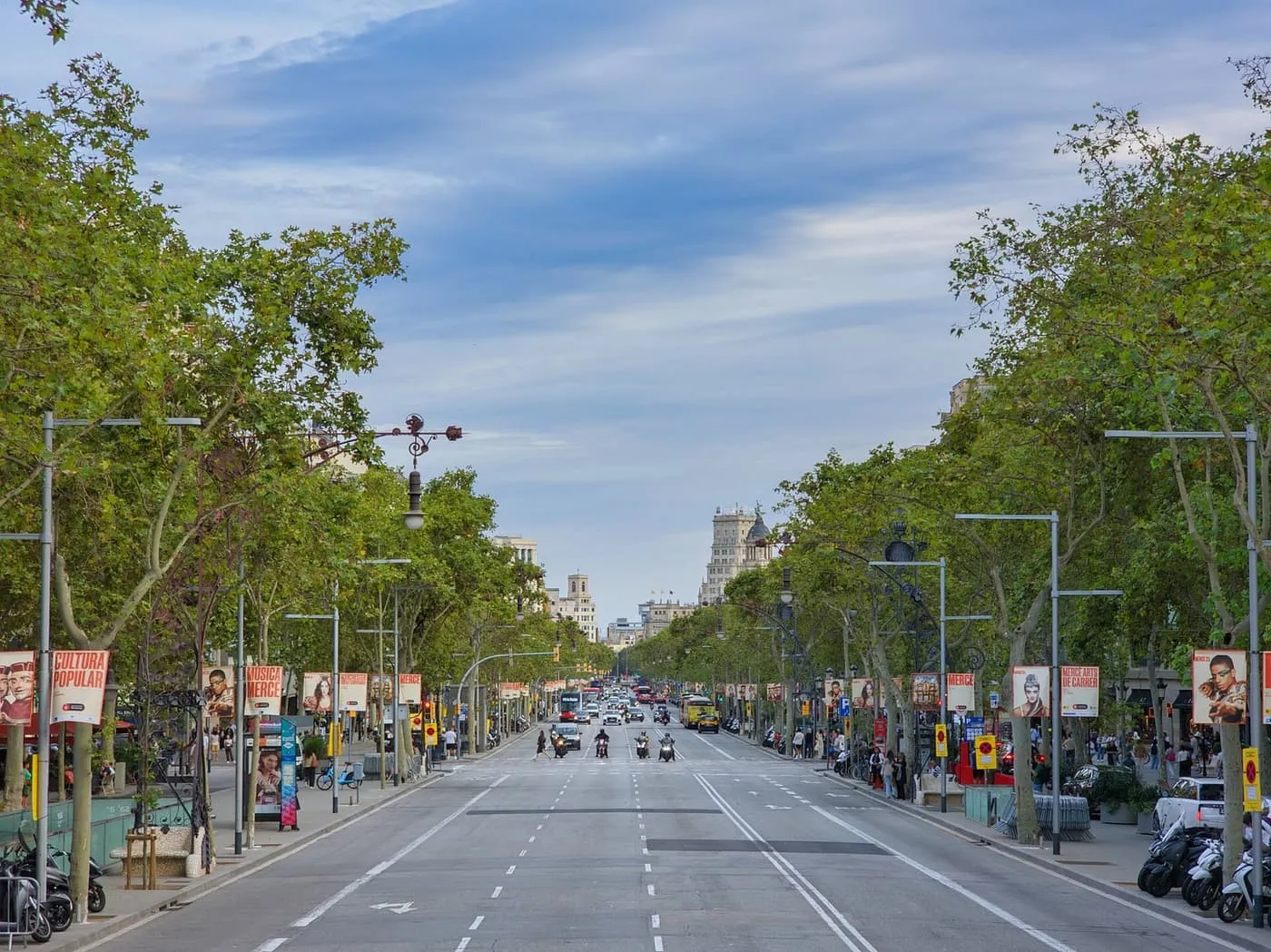 Passeig de Gràcia, a wide avenue lined with plane trees and ornate iron lamp posts, looking down towards the city centre