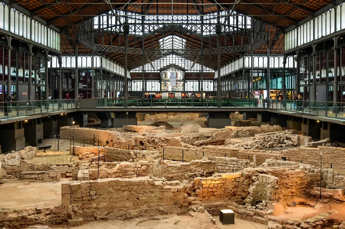 The iron-framed hall of the old El Born market, with a roof of tiles and glass above the excavated walls and streets of houses below