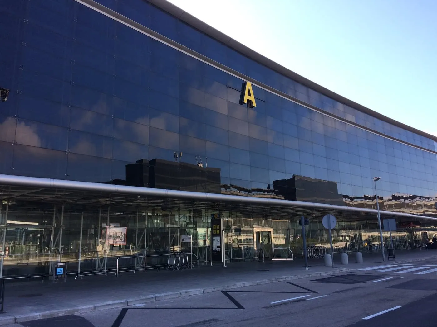 The long mirrored-glass front of Terminal 2A at Barcelona–El Prat, with a large yellow letter A above the entrance