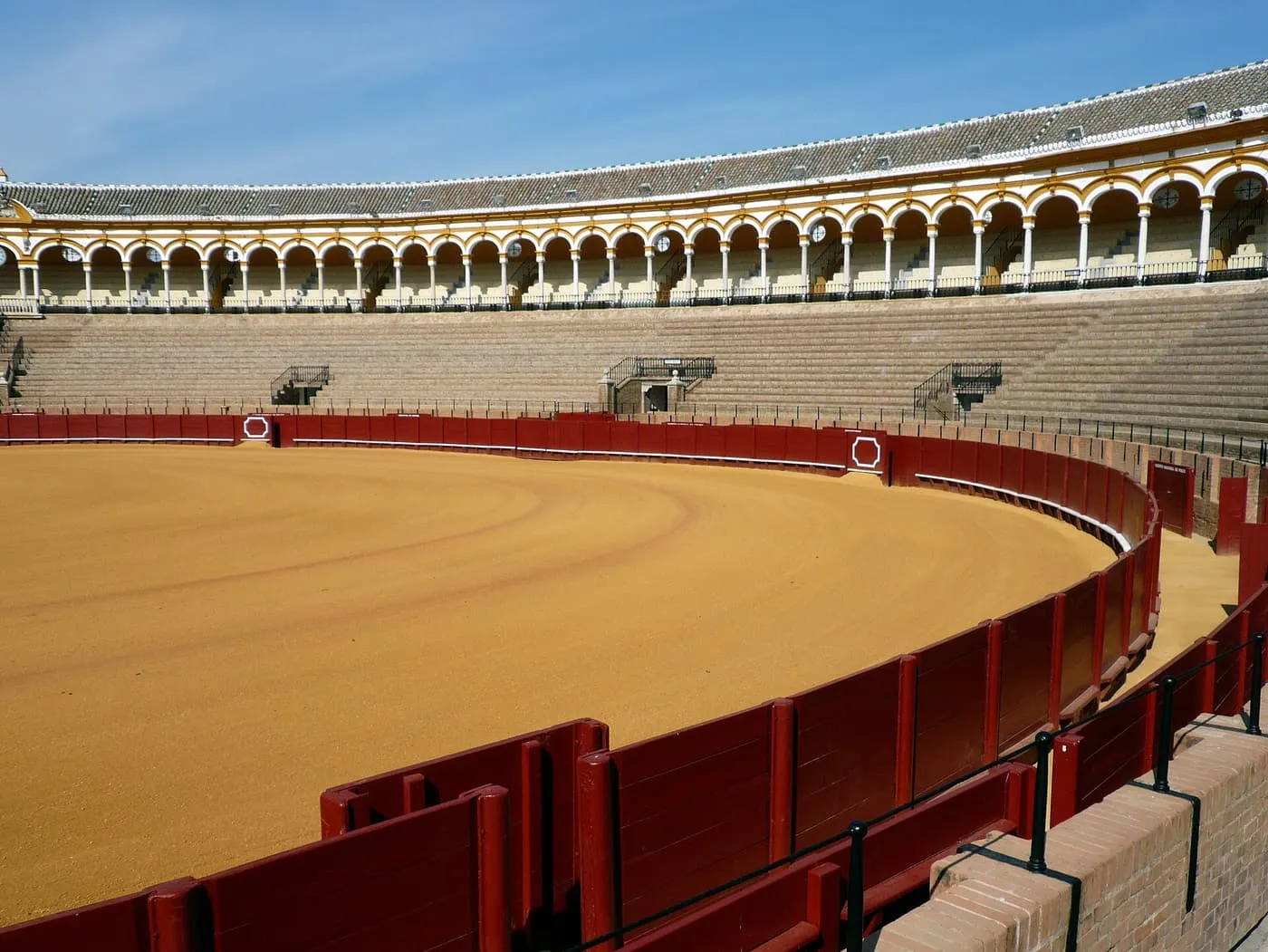 The empty sand arena of the Maestranza, with its red barrier and the white and yellow arcades of the stands