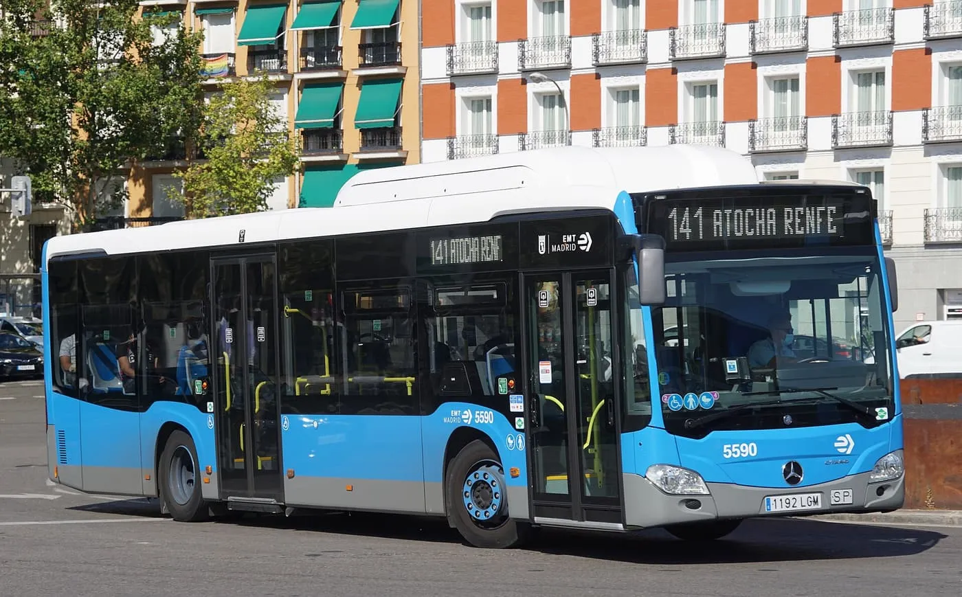 A blue and white EMT city bus on the 141 route to Atocha Renfe, in front of apartment blocks