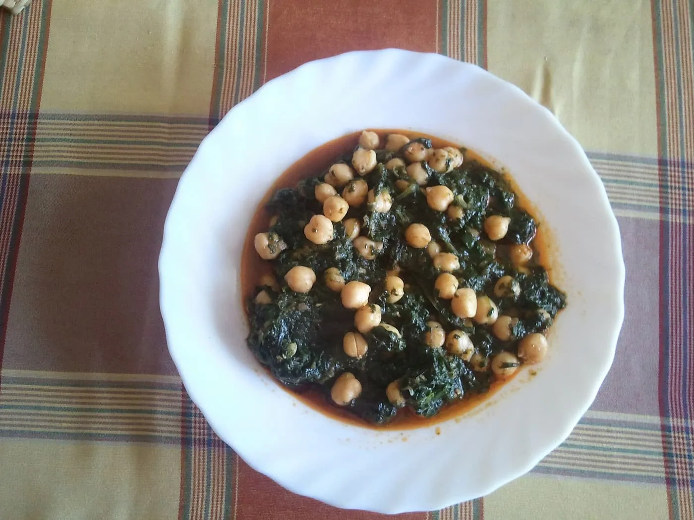 A white bowl of spinach with chickpeas in a dark sauce