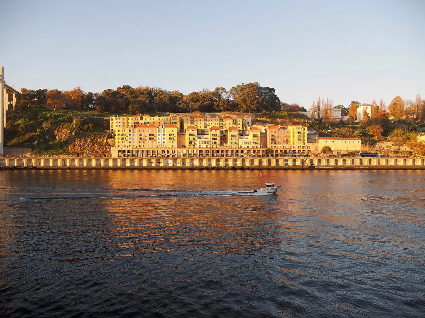 A small motorboat crossing the Douro in warm evening light, with a row of pale apartment buildings on the far bank