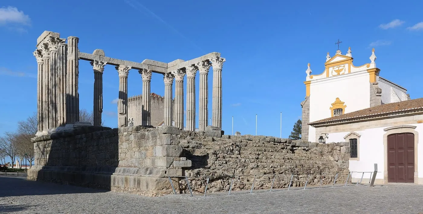 The Corinthian columns of Évora's Roman temple on its stone base, beside a white church with yellow trim