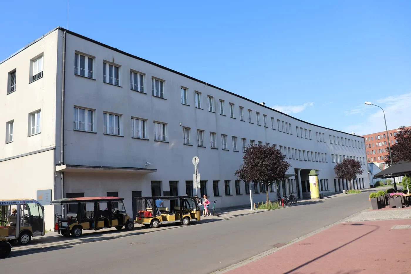 The curved white front of the former administrative building of Oskar Schindler's enamel factory on ul. Lipowa, with golf carts parked outside
