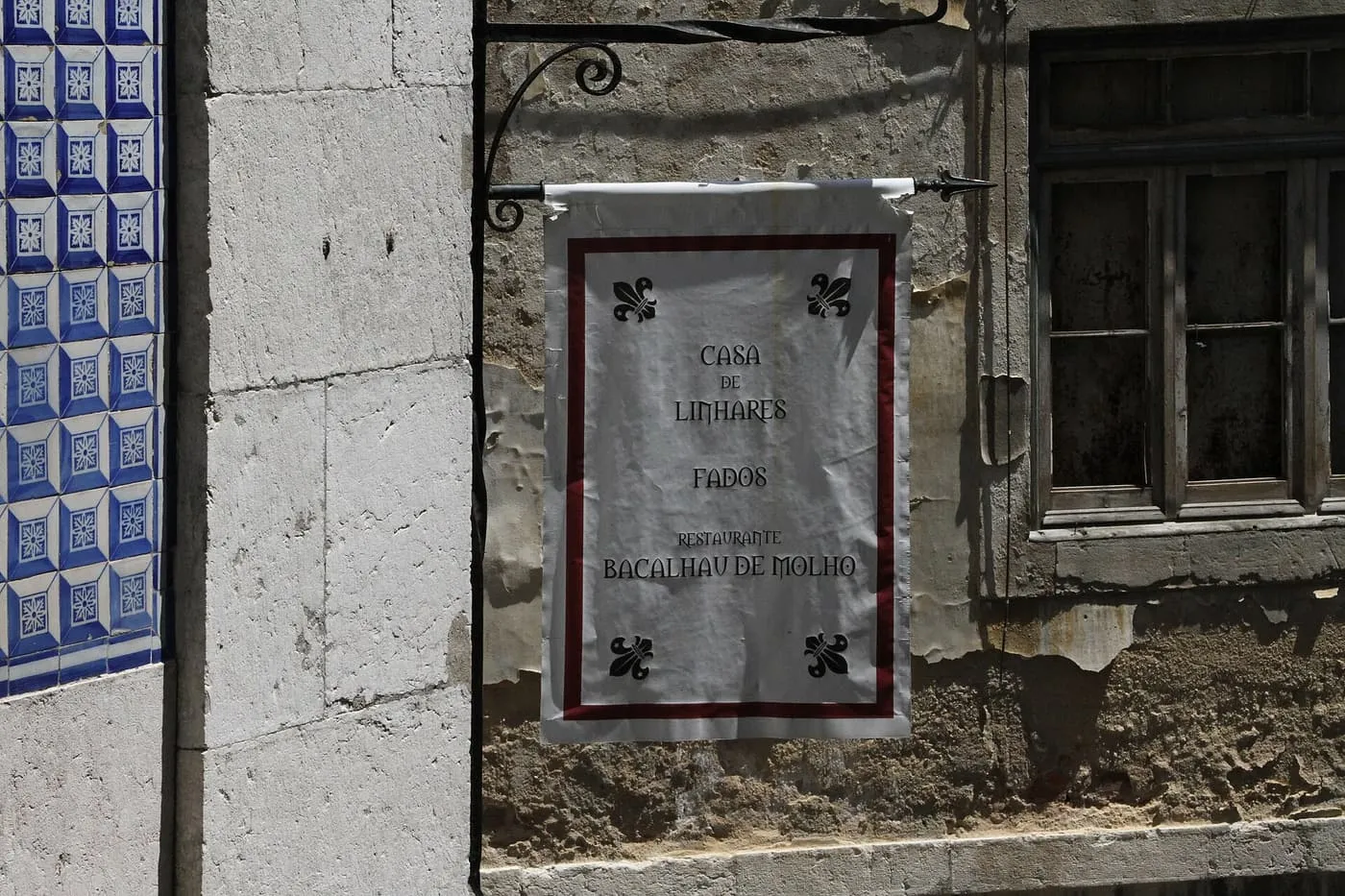 A white hanging sign reading Fados and Restaurante Bacalhau de Molho, beside a blue and white tiled wall in Alfama