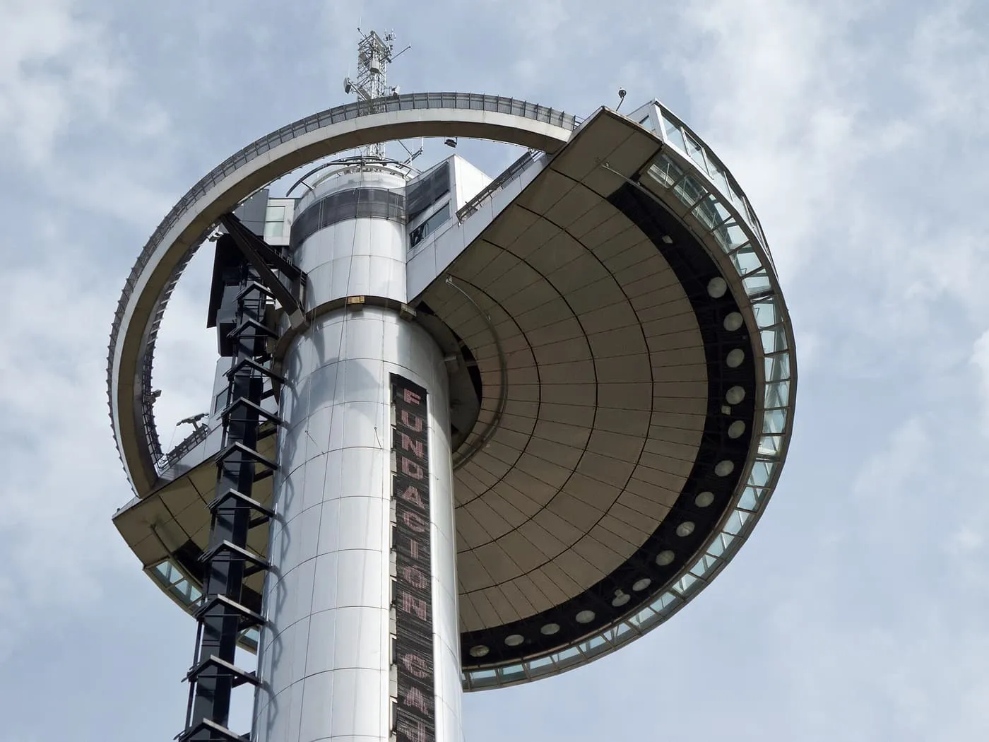 The circular observation deck of the Faro de Moncloa at the top of its silver tower, seen from below against a pale sky