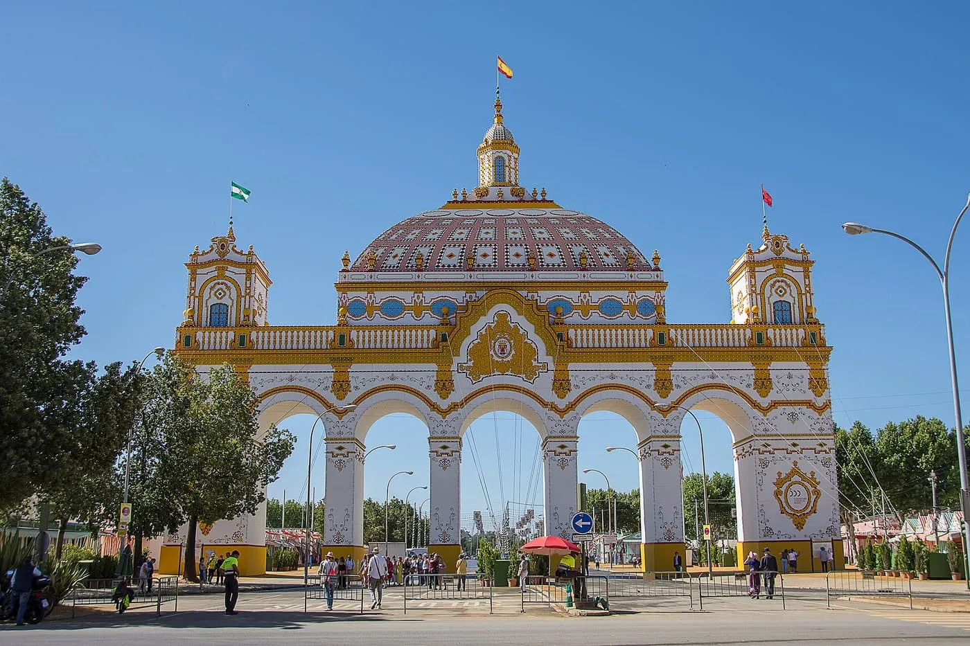 The Feria de Abril entrance arch, a white and gold arcade with a domed centre and two towers under a blue sky