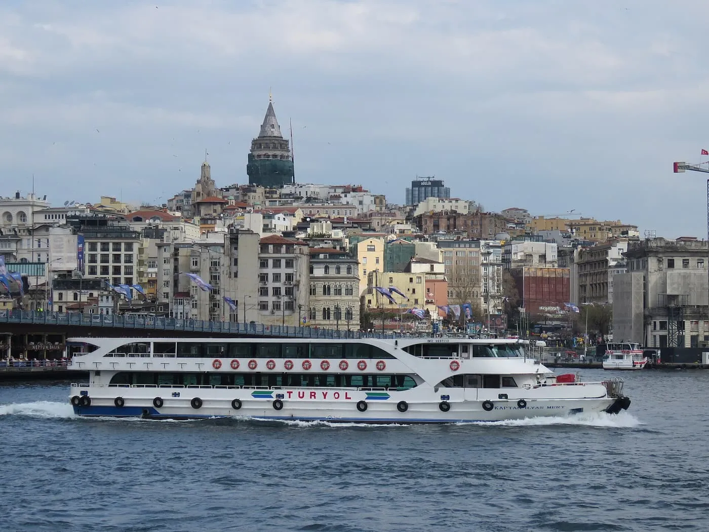 A white ferry passing in front of the Galata Bridge, with the Galata Tower above the buildings of Karaköy