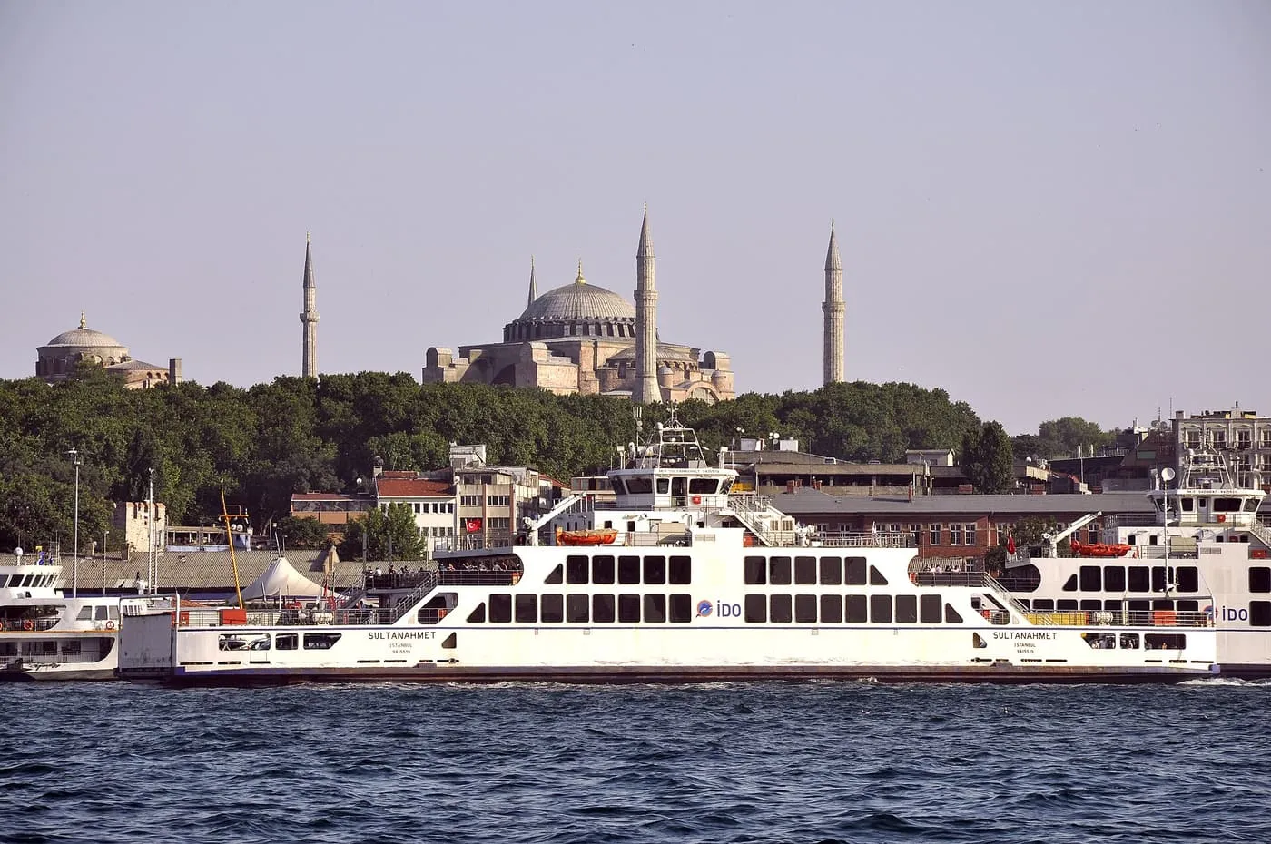 A white passenger and car ferry crossing in front of the old city, with Hagia Sophia and its minarets on the skyline behind