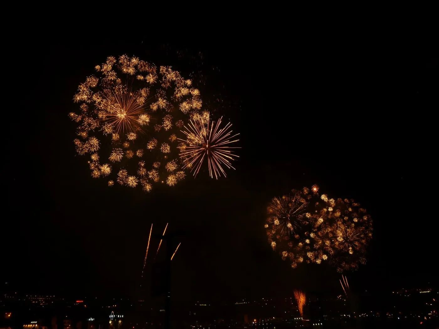 Gold fireworks bursting in a black sky above the lights of the city