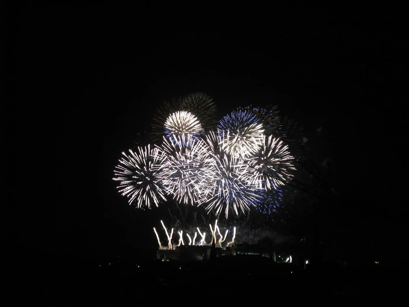 White and blue fireworks bursting in the night sky over Edinburgh at New Year