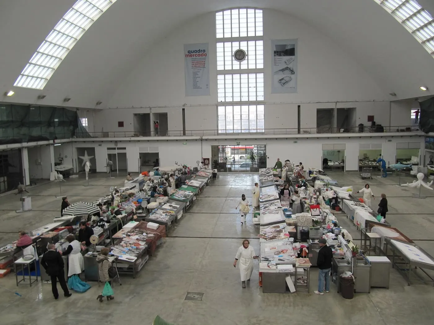 The vaulted hall of the Matosinhos fish market, with rows of stalls on both sides and shoppers and stallholders between them