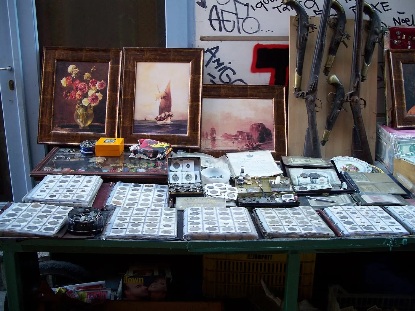 A street stall at the Monastiraki flea market, with albums of old coins, banknotes, framed prints and antique flintlock pistols