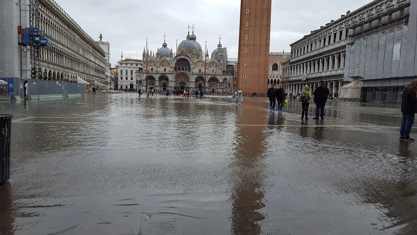 Water covering St Mark's Square, with the Basilica and the Campanile at the far end and a few people walking through it