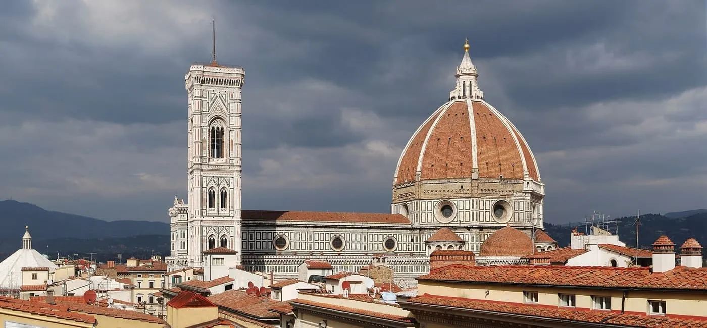 Florence Cathedral's dome and Giotto's bell tower against dark clouds, seen over the rooftops