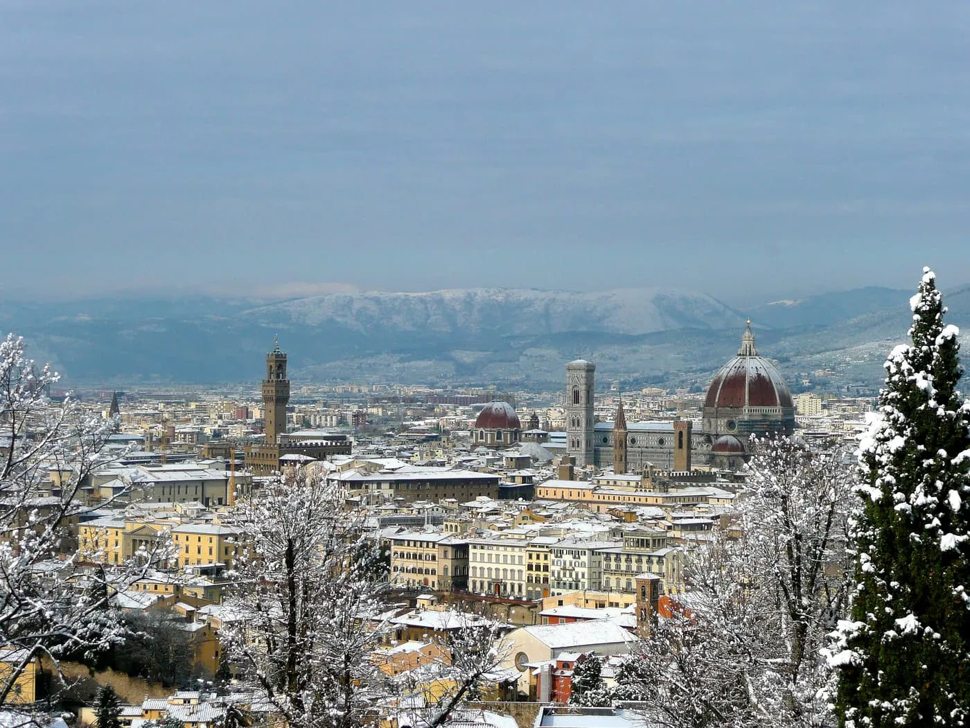 Florence under snow, with the Duomo dome and the tower of Palazzo Vecchio above white roofs and snowy trees