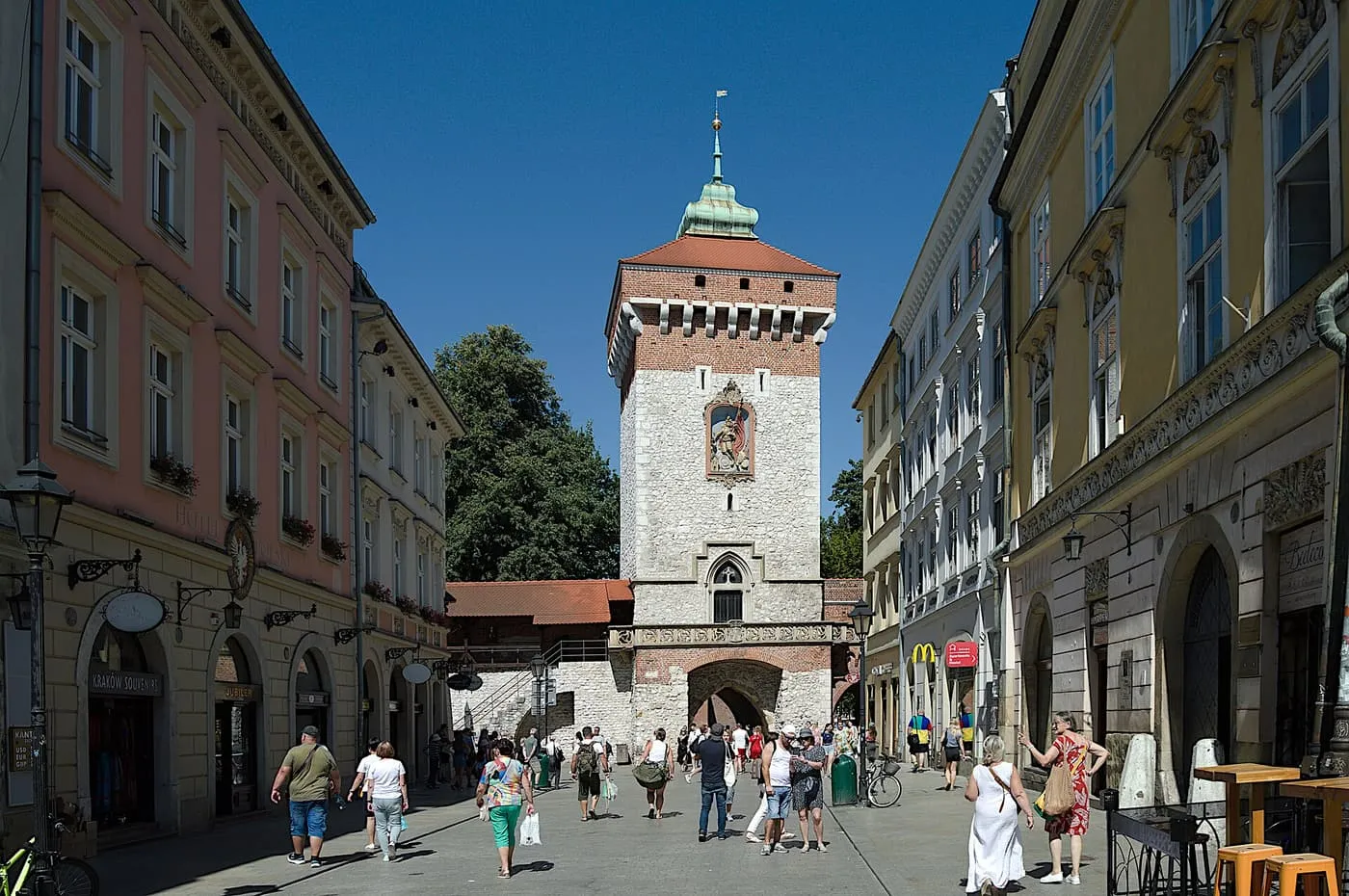 St Florian's Gate, a tall stone and brick tower with a green Baroque cap, seen down Floriańska Street with people walking towards it