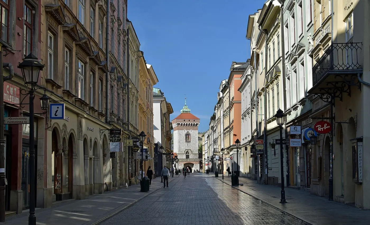 Floriańska Street, a cobbled street of tall townhouses with lamps and shop signs, running straight to the stone tower of St Florian's Gate