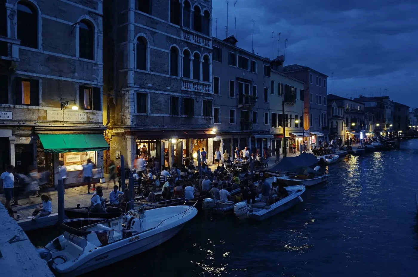 Tables along the Fondamenta degli Ormesini at dusk, with people drinking beside the canal and boats moored alongside