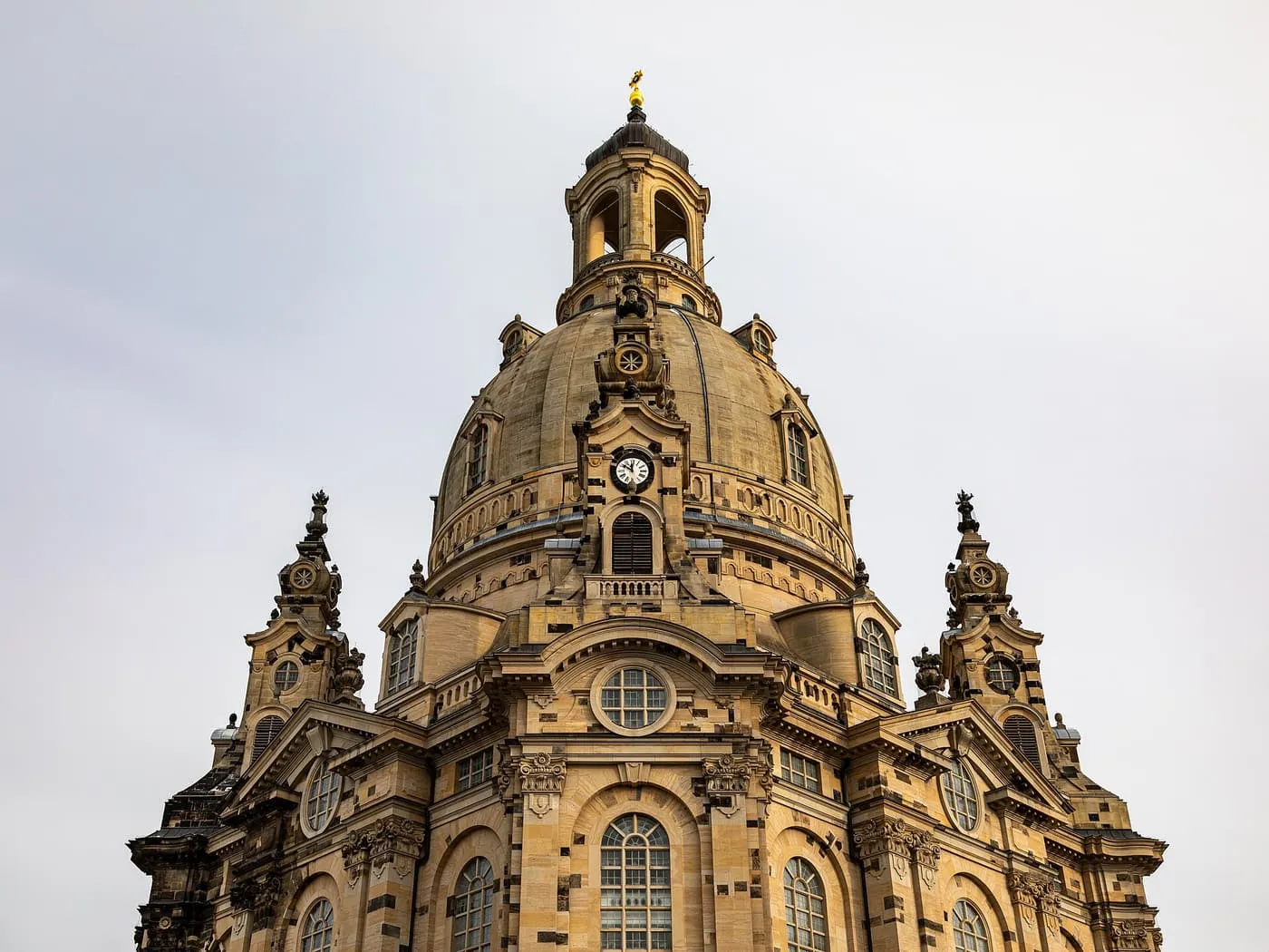 The stone dome and lantern of the Frauenkirche in Dresden, with a clock face and carved pinnacles on the roofline
