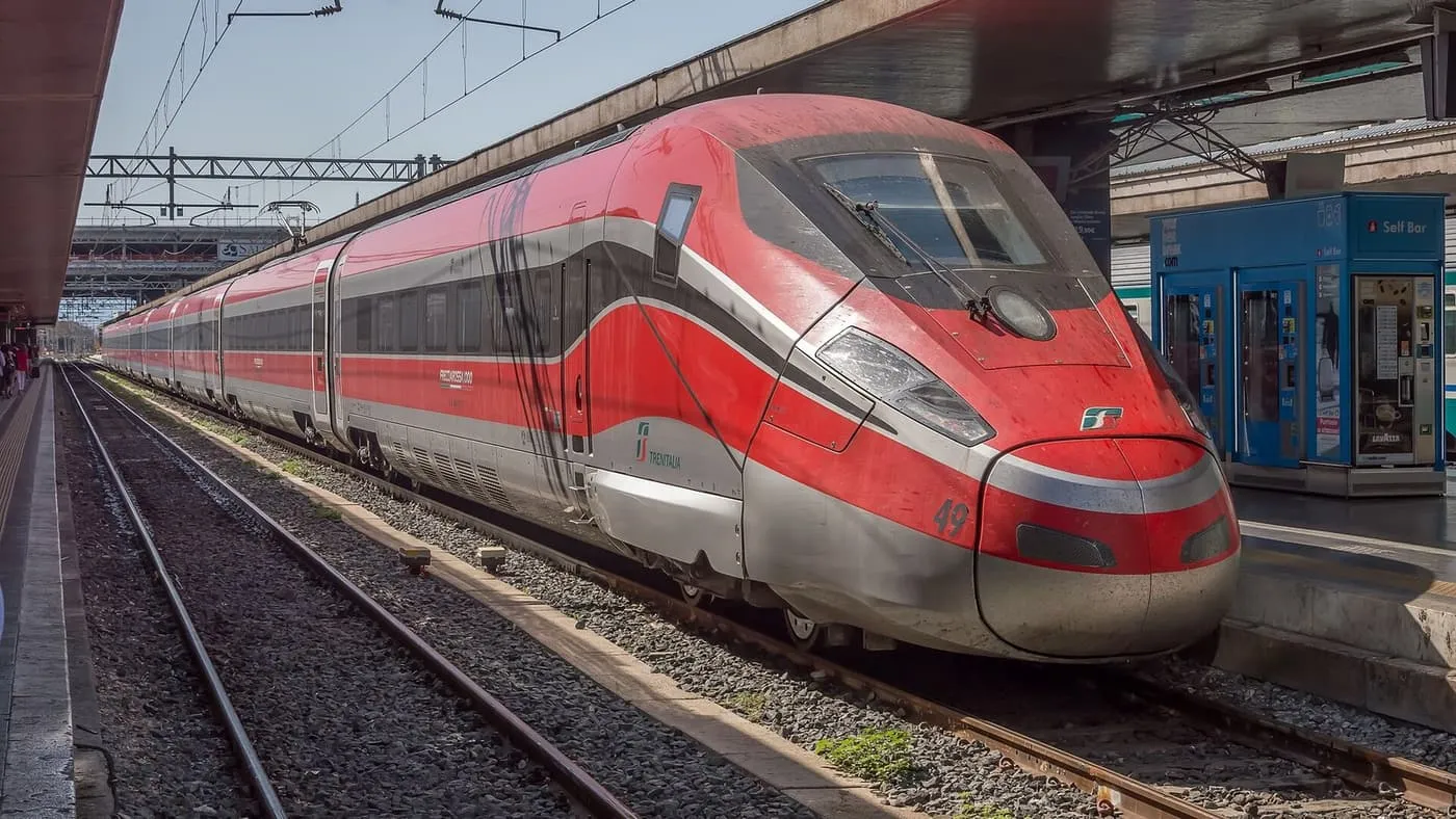 A red Frecciarossa 1000 high-speed train at a platform at Roma Termini, with the station name on blue signs behind it