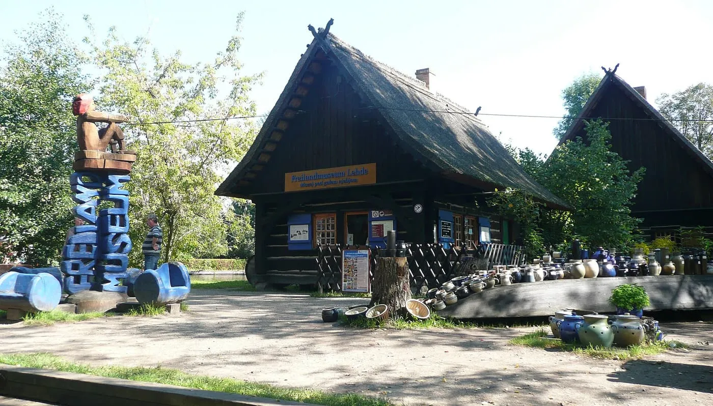 A thatched log building with a Freilandmuseum Lehde sign, with pottery displayed in front of it