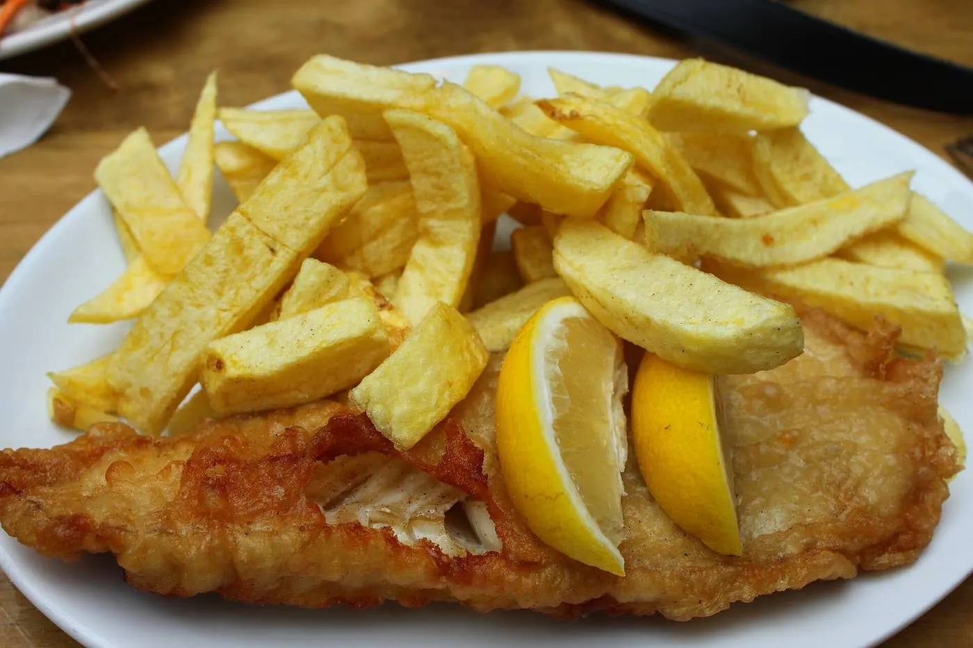 A plate of battered fried cod with thick-cut chips and two lemon wedges