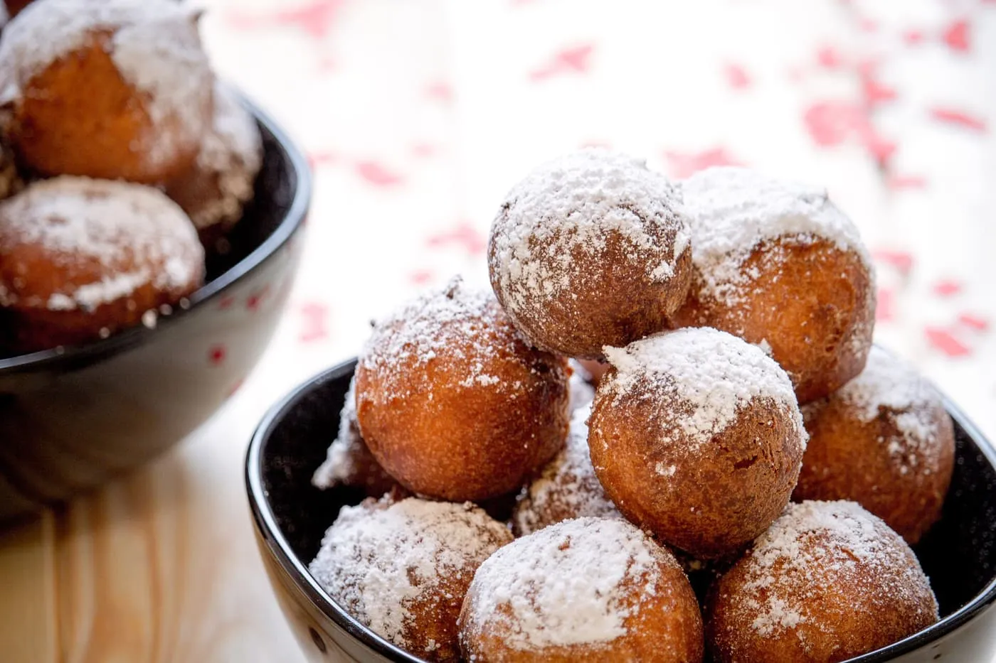 Fried dough balls dusted with icing sugar, piled in black bowls