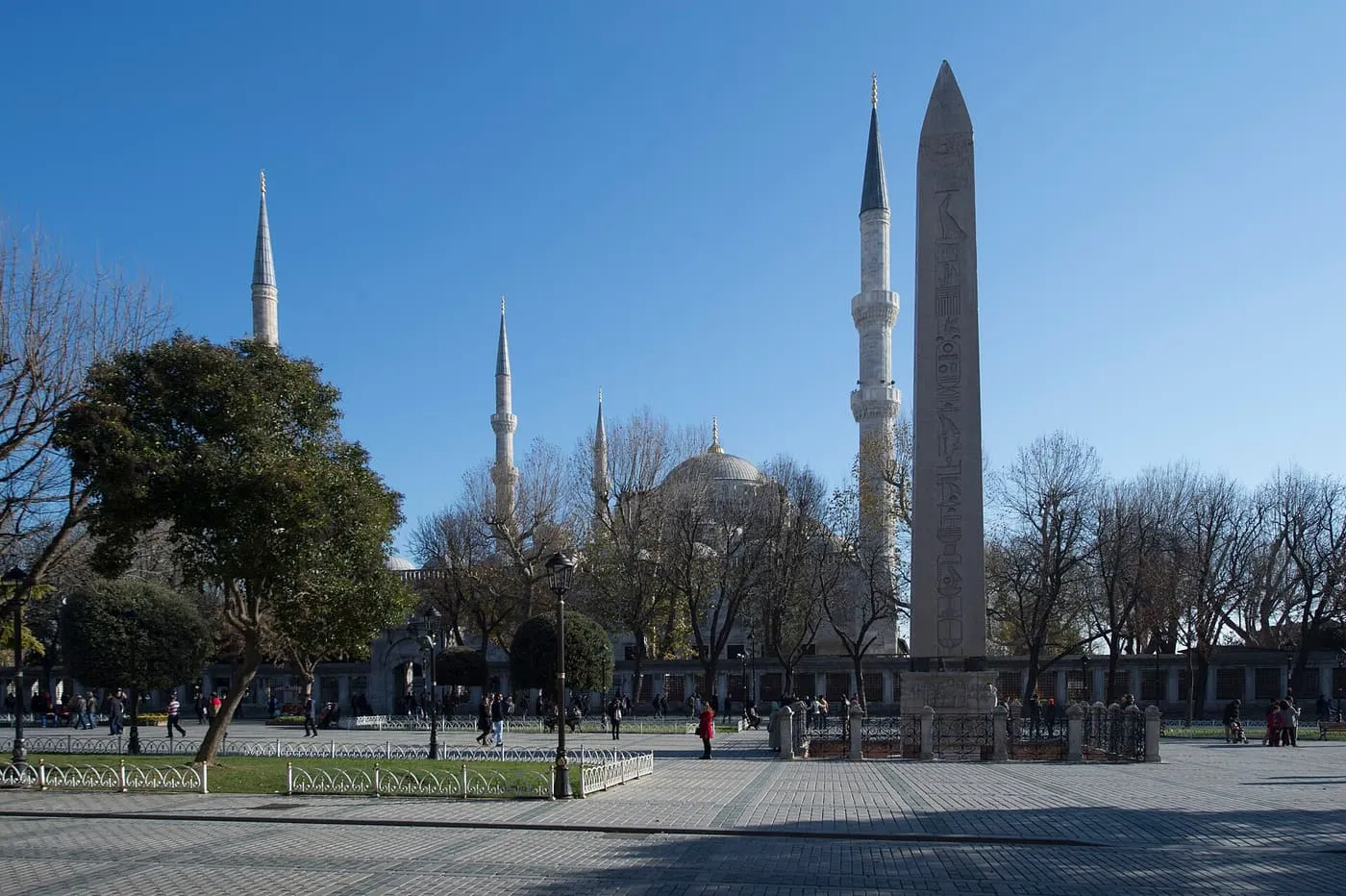 The Blue Mosque's minarets and domes rising behind trees on the Hippodrome, with the Egyptian obelisk standing at the right