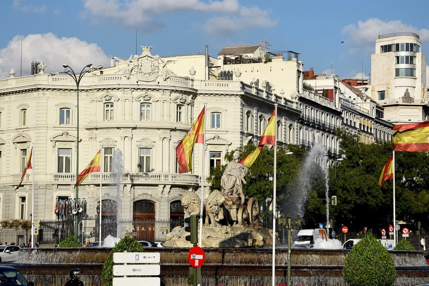 The Fuente de Cibeles, with the goddess in her lion-drawn chariot and jets of water, in front of the Palacio de Linares and Spanish flags