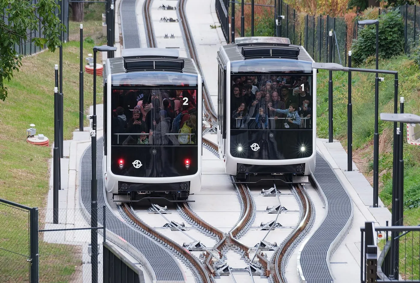 Two glazed funicular cars passing on the Petřín line, one numbered 1 and one numbered 2, with passengers at the front windows