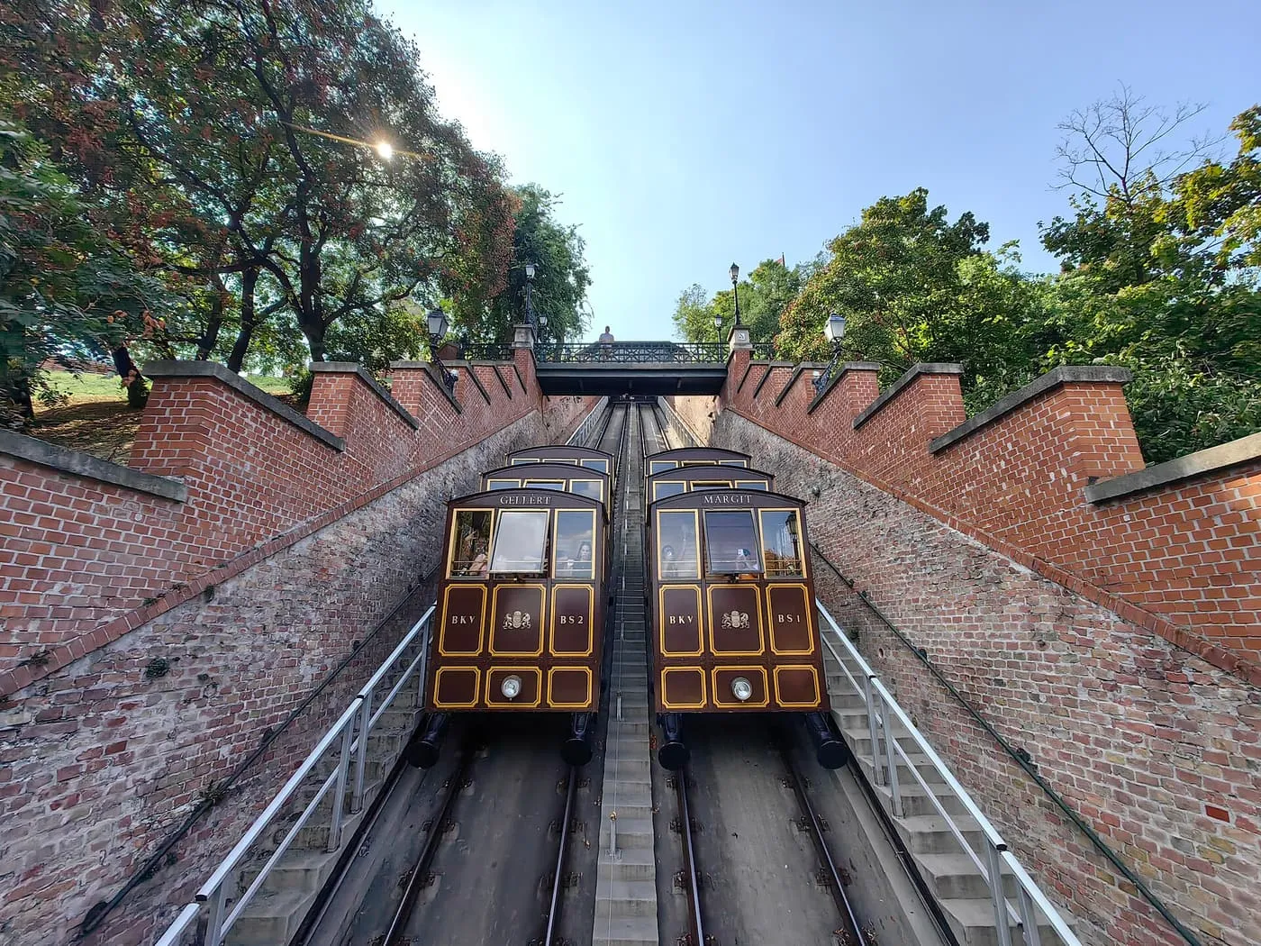 The two cars of the Buda Castle Funicular side by side on a steep track between brick walls